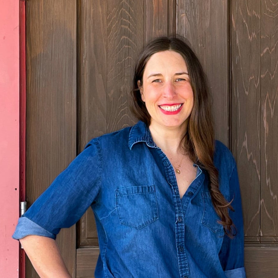 Fine artist Lucile Wedeking standing in front of a wooden door with a red frame.